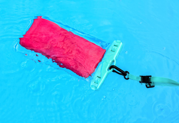Από πάνω κινητό τηλέφωνο σε διαφανή αδιάβροχη θήκη που επιπλέει σε διάφανο νερό της πισίνας - Φωτογραφία, εικόνα