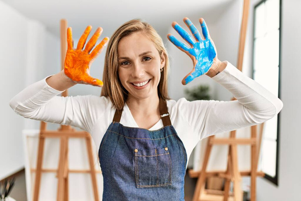 Young caucasian woman smiling confident showing painted palm hands at art studio - Fotó, kép