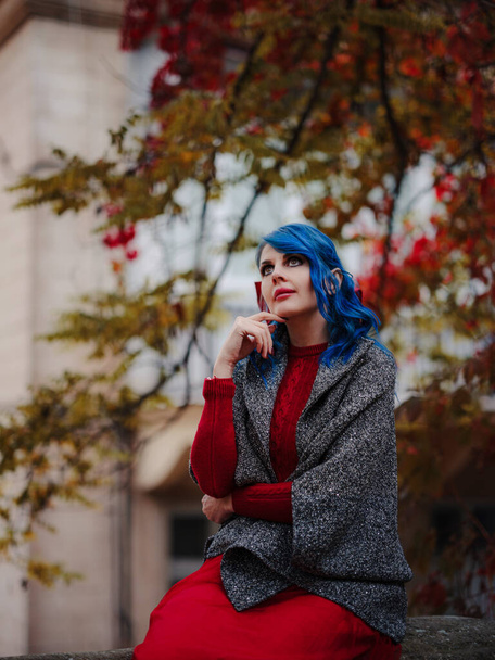 season and people concept . Autumn portrait of woman with blue hair, red dress and gray cape. Outdoor beauty portrait of walk through city after rain. - Foto, imagen