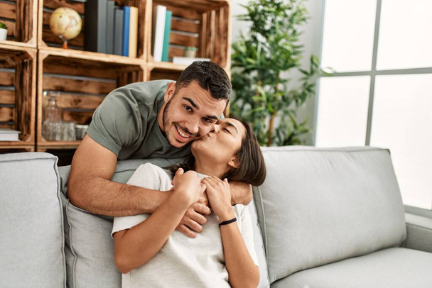 Young latin couple sitting on the sofa hugging at home. - 写真・画像