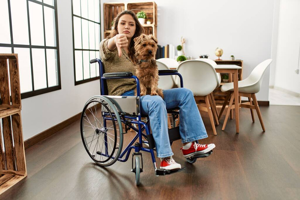 Jeune fille hispanique assise en fauteuil roulant à la maison souriant amical offrant poignée de main comme salutation et accueil. entreprise prospère.  - Photo, image