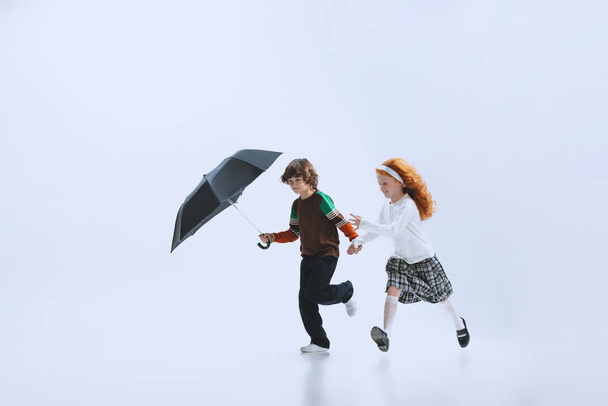 Two happy kids, boy and girl running with umbrella isolated on white studio background. Childhood, dreams, imagination, education - Φωτογραφία, εικόνα