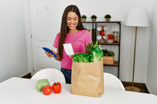 Young latin woman calcultating prize of groceries bag at home - Foto, immagini
