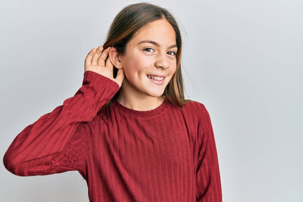 Красивая брюнетка маленькая девочка в случайном свитере улыбается с рукой над ухом слушая и слушая слухи или сплетни. концепция глухоты.  - Фото, изображение