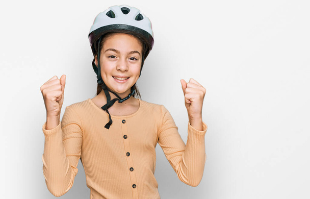Hermosa niña morena con casco de bicicleta gritando orgulloso, celebrando la victoria y el éxito muy emocionado con los brazos levantados  - Foto, Imagen