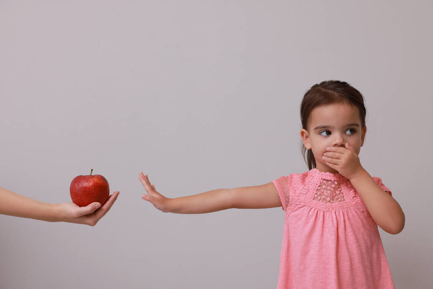 Cute little girl covering mouth and refusing to eat apple on grey background - Zdjęcie, obraz