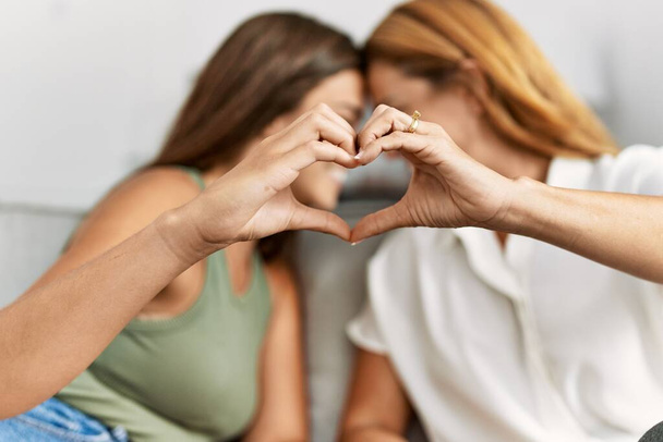 Mother and daughter smiling confident make heart gesture with hands at home - Foto, Imagem