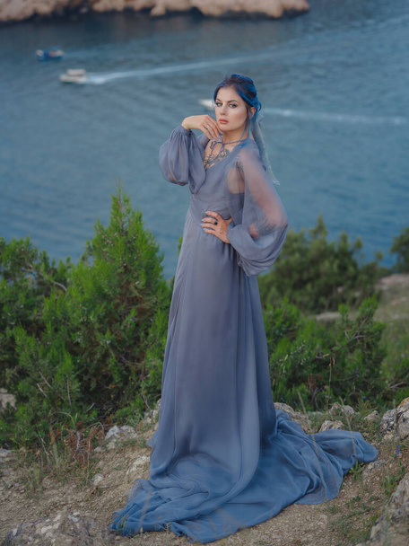 Young beautiful woman with blue hair in gray dress looking at the sea mountains. Lady in nature. Fashion photos. Silk Cloth Waving on Wind - Photo, Image