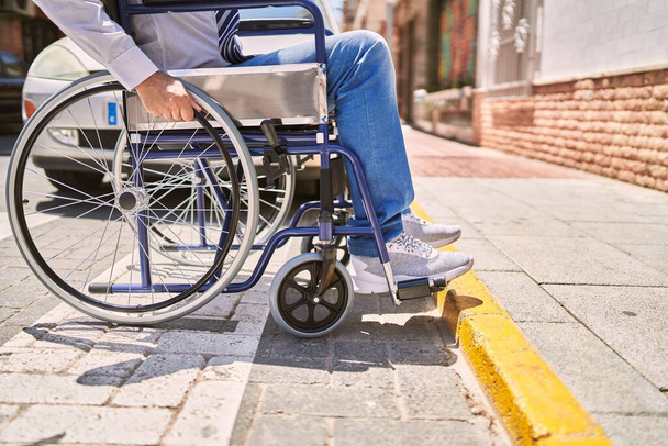 Uomo ispanico di mezza età che indossa abiti da lavoro seduto sulla sedia a rotelle in strada - Foto, immagini