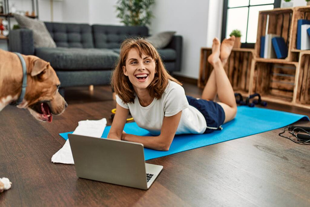 Young caucasian woman sportswoman smiling confident using laptop with dog at home - Foto, immagini