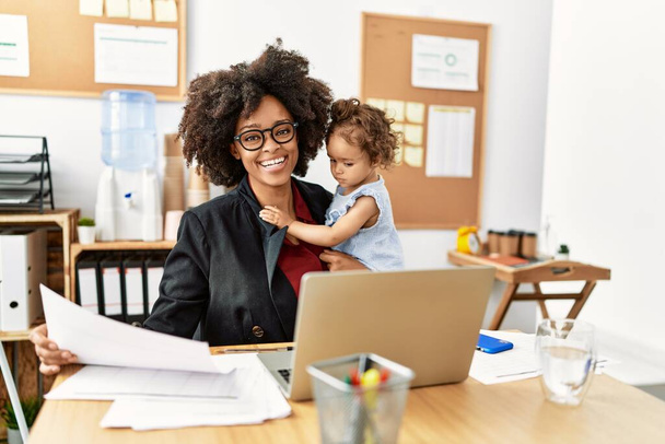 Mujer afroamericana joven sonriendo confiada trabajando con el bebé en la oficina - Foto, imagen