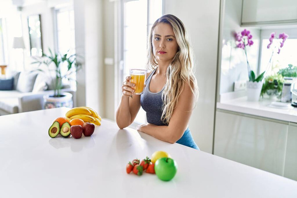 Young caucasian fitness woman wearing sportswear drinking healthy orange juice thinking attitude and sober expression looking self confident  - Foto, immagini