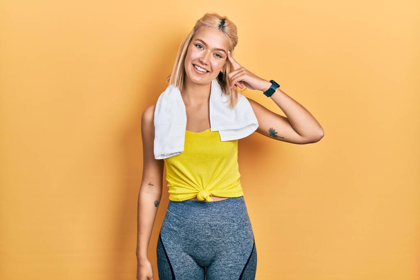 Krásná blondýnka sportovní žena na sobě cvičení oblečení s úsměvem ukazuje na hlavu s jedním prstem, skvělý nápad nebo myšlenka, dobrá paměť  - Fotografie, Obrázek