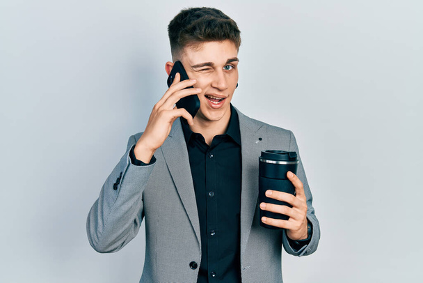 Young caucasian boy with ears dilation using smartphone and drinking a cup of coffee winking looking at the camera with sexy expression, cheerful and happy face.  - Φωτογραφία, εικόνα
