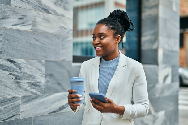 Young african american businesswoman using smartphone and drinking coffee at the city. - Φωτογραφία, εικόνα