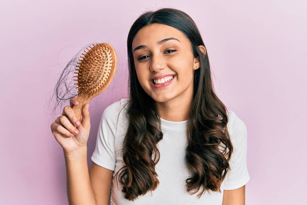 Jovem mulher hispânica styling cabelo usando pente olhando positivo e feliz de pé e sorrindo com um sorriso confiante mostrando dentes  - Foto, Imagem