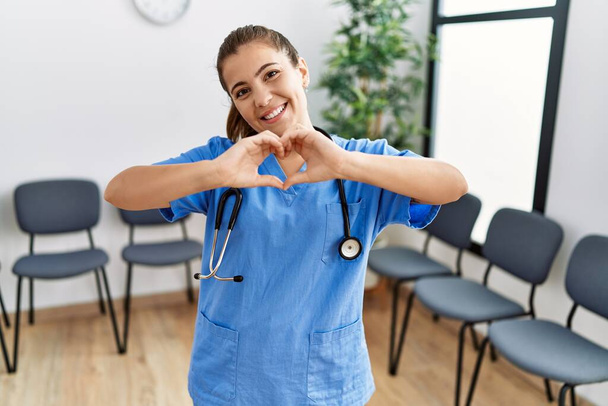 Young brunette doctor woman at waiting room smiling in love showing heart symbol and shape with hands. romantic concept.  - Photo, Image