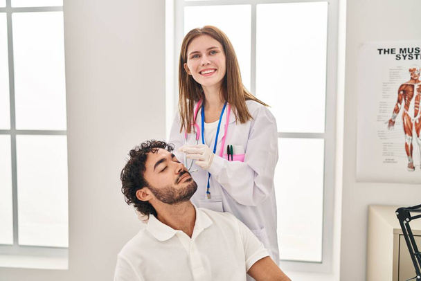 Man and woman wearing doctor uniform applying eye drops at clinic - Foto, afbeelding