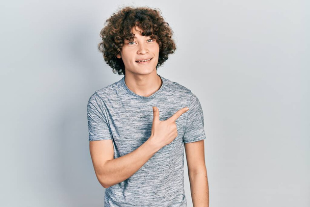 Handsome young man wearing casual grey t shirt smiling cheerful pointing with hand and finger up to the side  - Foto, afbeelding