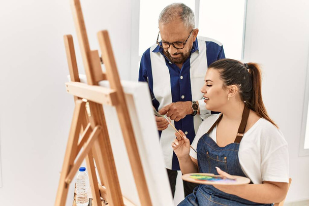 Senior Mallehrer Mann unterrichtet junge Frau beim Malen auf Leinwand im Kunstatelier - Foto, Bild