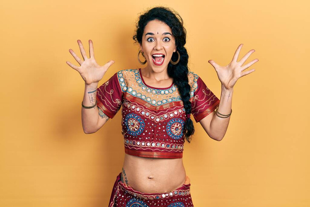 Junge Frau in Bindi- und Bollywood-Kleidung feiert verrückt und erstaunt über den Erfolg mit erhobenen Armen und offenen Augen, die aufgeregt schreien. Siegerkonzept  - Foto, Bild