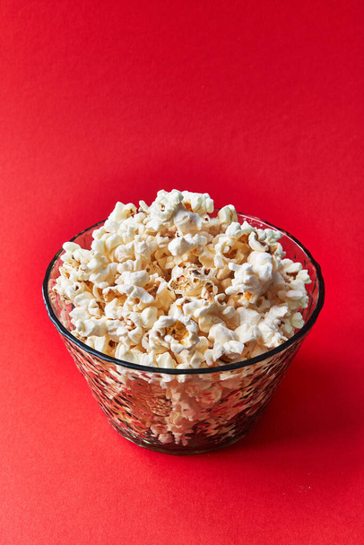 Schaal van zoute popcorn op een rode achtergrond - Foto, afbeelding