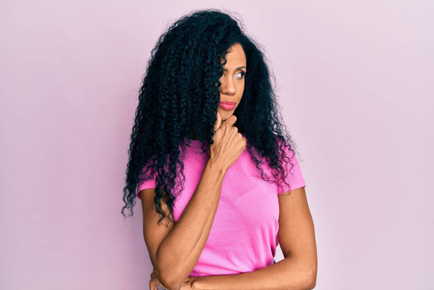 Middle age african american woman wearing casual clothes with hand on chin thinking about question, pensive expression. smiling with thoughtful face. doubt concept.  - Photo, Image