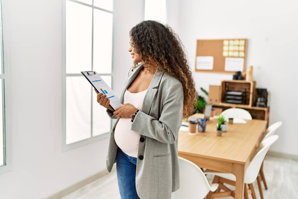 Giovane donna latina incinta sorridente fiducioso tenendo appunti in ufficio - Foto, immagini