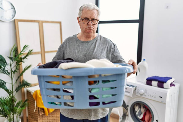 Vanhempi valkoihoinen mies pitelee pesuainepulloa pesutuvassa rentoutuneena vakavalla ilmeellä. yksinkertainen ja luonnollinen kameraan katsominen.  - Valokuva, kuva
