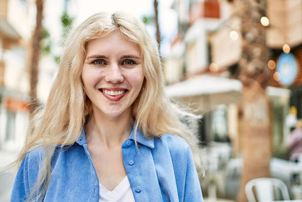 Schöne blonde junge Frau lächelt glücklich draußen an einem sonnigen Tag - Foto, Bild