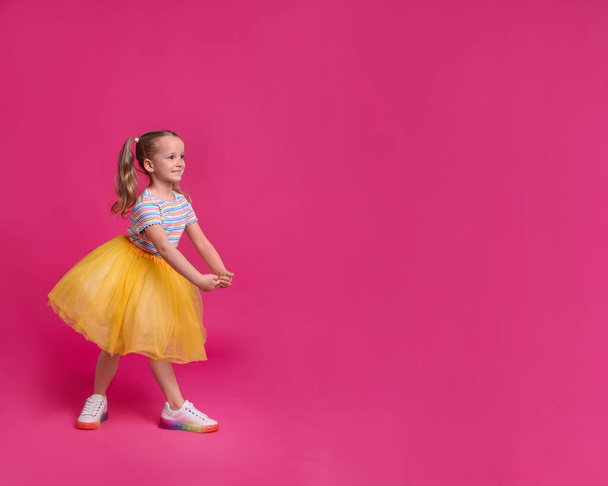 Cute little girl in tutu skirt dancing on pink background. space for text - Foto, Imagen
