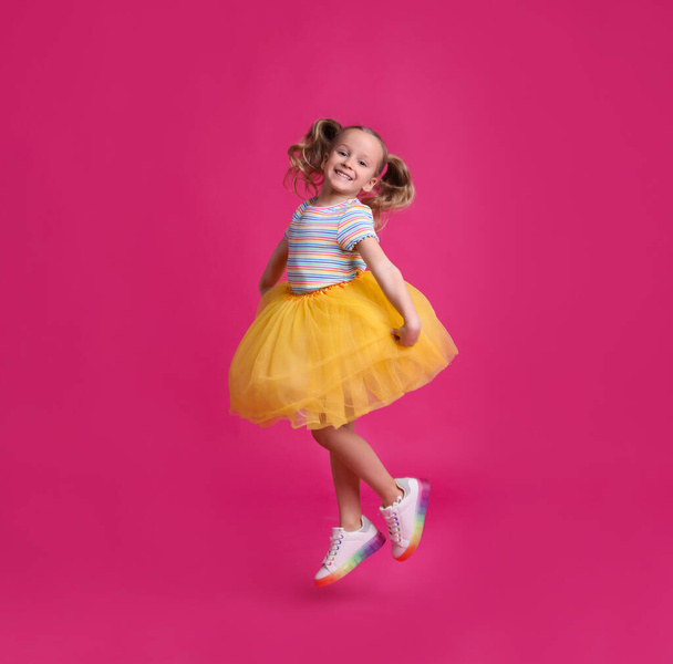 Cute little dancer in tutu skirt jumping on pink background - Photo, Image