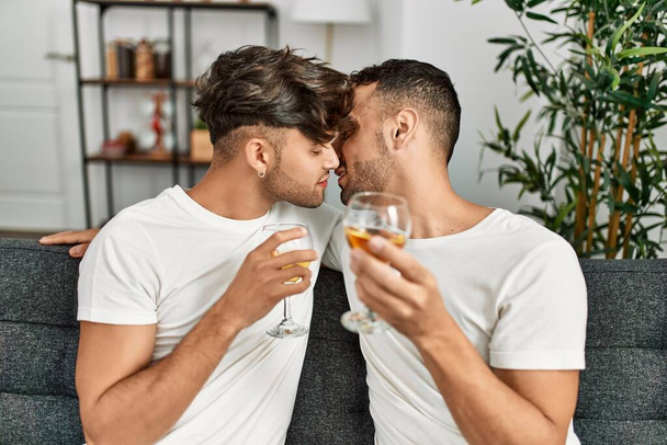 Twee Spaanse mannen paar zoenen en toasten met glas wijn thuis - Foto, afbeelding