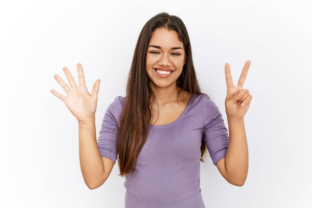 Nuori brunette nainen seisoo eristetty tausta näyttää ja osoittaa sormilla numero seitsemän hymyillen itsevarma ja onnellinen.  - Valokuva, kuva