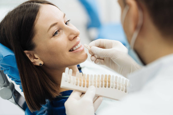 Dişçi genç kadın dişlerinin rengini kontrol ediyor ve seçiyor - Fotoğraf, Görsel