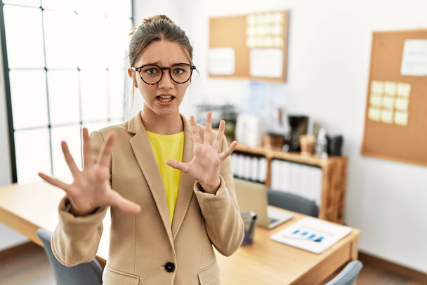 Junge brünette Teenager tragen Business-Stil im Büro Angst und Angst mit Angst Ausdruck Stop-Geste mit den Händen, schreien vor Schreck. Panikkonzept.  - Foto, Bild