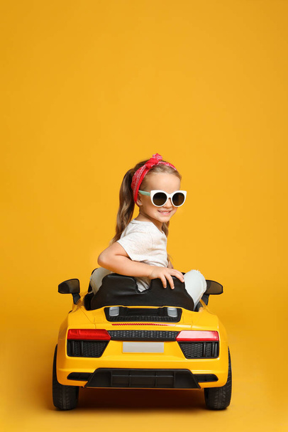 Cute little girl driving children's electric toy car on yellow background - Fotó, kép