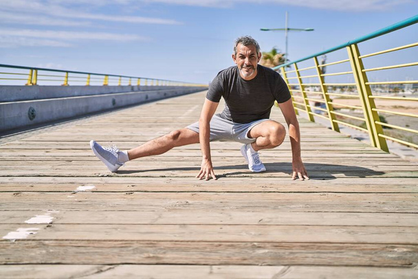 Middle age hispanic man wearing sportswear stretching at street - Photo, Image