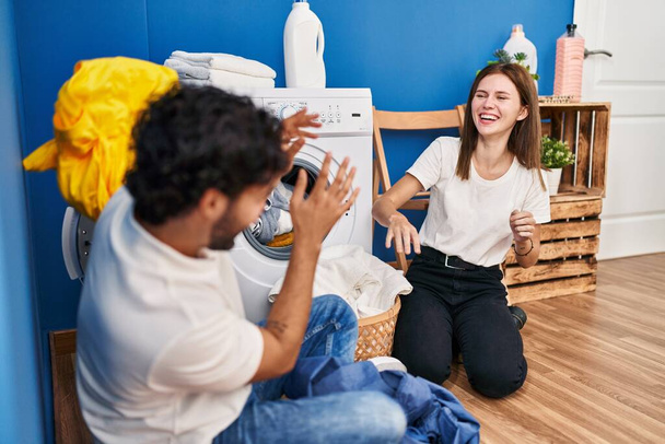 man en vrouw paar glimlachen zelfverzekerd spelen met schoonmaak kleding in wasruimte - Foto, afbeelding