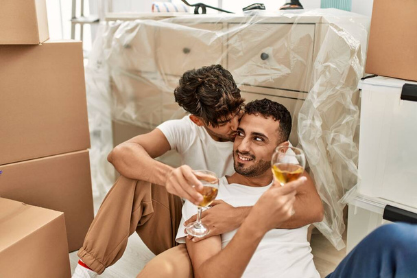 Two hispanic men couple smiling confident drinking wine at new home - Foto, afbeelding