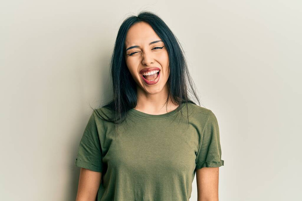 Fiatal spanyol lány visel alkalmi póló kacsintás a kamerába szexi kifejezés, vidám és boldog arc.  - Fotó, kép