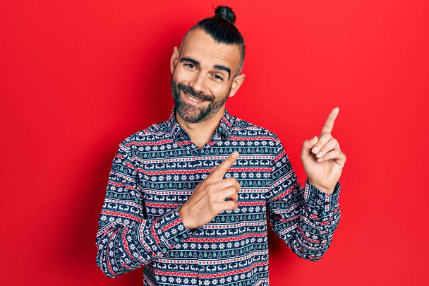Young hispanic man wearing casual clothes smiling and looking at the camera pointing with two hands and fingers to the side.  - Foto, afbeelding