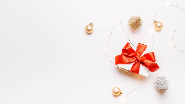 Karácsonyi ajándék. Fehér ajándék piros íj, arany golyók és csillogó fények koszorú Xmas dekoráció fehér háttér üdvözlő kártya. Karácsonyi háttér helyet a szöveges - Fotó, kép