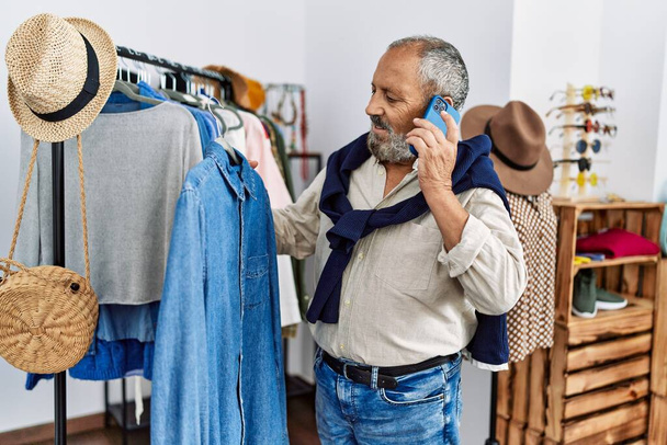 Старший седовласый мужчина с рубашкой разговаривает по смартфону в магазине одежды - Фото, изображение