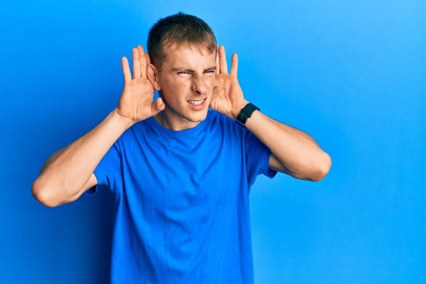 Young caucasian man wearing casual blue t shirt trying to hear both hands on ear gesture, curious for gossip. hearing problem, deaf  - Zdjęcie, obraz