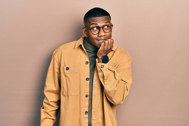 Young black man wearing casual clothes and glasses looking stressed and nervous with hands on mouth biting nails. anxiety problem.  - Photo, Image