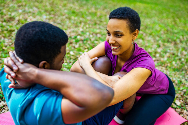 Strong and powerful afro american couple in love are working out abs exercises outside in park or forest - Fotó, kép