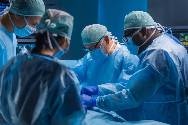 Multiracial team of professional medical surgeons performs the surgical operation in a modern hospital. Doctors are working to save the patient. Medicine, health, cardiology and transplantation. - 写真・画像