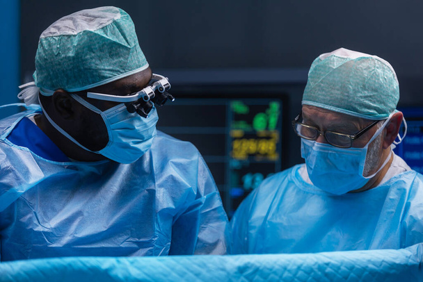 Multiracial team of professional medical surgeons performs the surgical operation in a modern hospital. Doctors are working to save the patient. Medicine, health and neurosurgery. - Foto, Bild