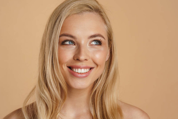 Beauty image of a smiling happy young blonde woman with long hair naked shoulders standing over beige background - Foto, immagini